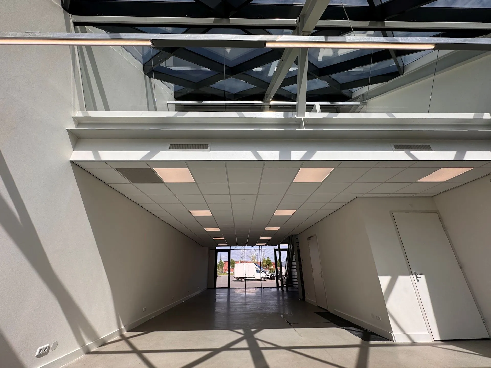 Lichte en moderne gang in het Mart Stamhof gebouw met glazen plafond en schaduwwerking.